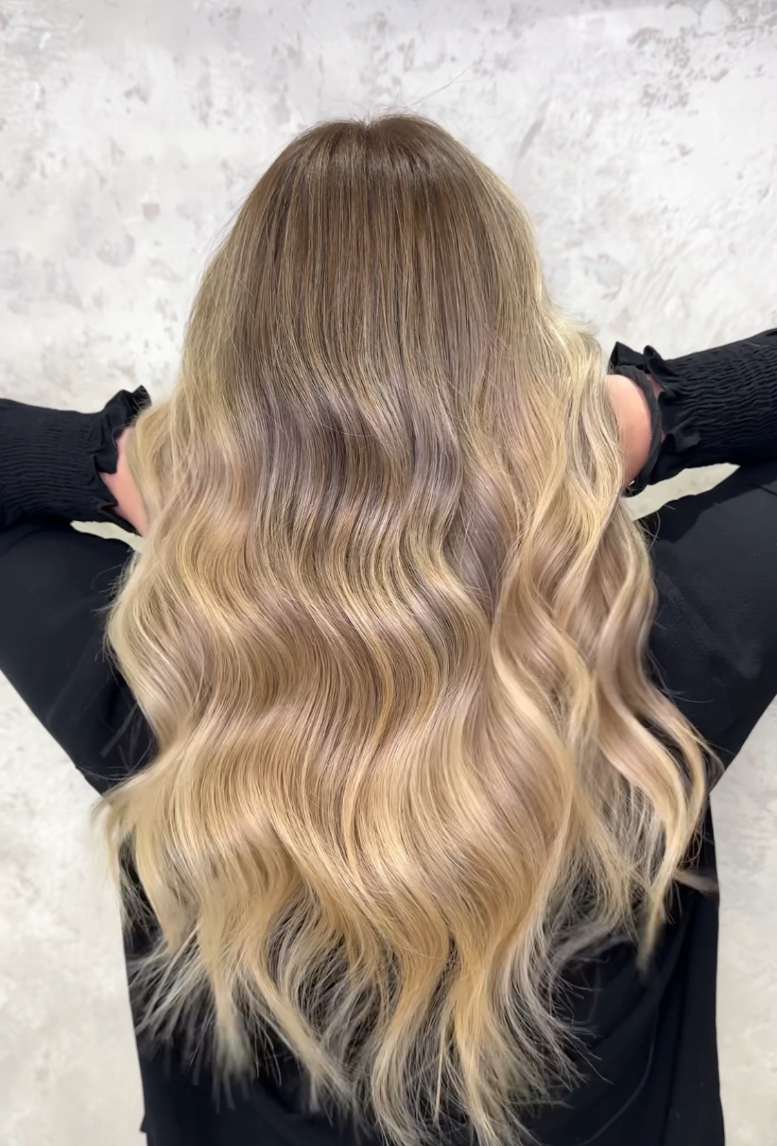 Goudblonde balayage met zachte golven, gefotografeerd tegen een marmeren achtergrond
